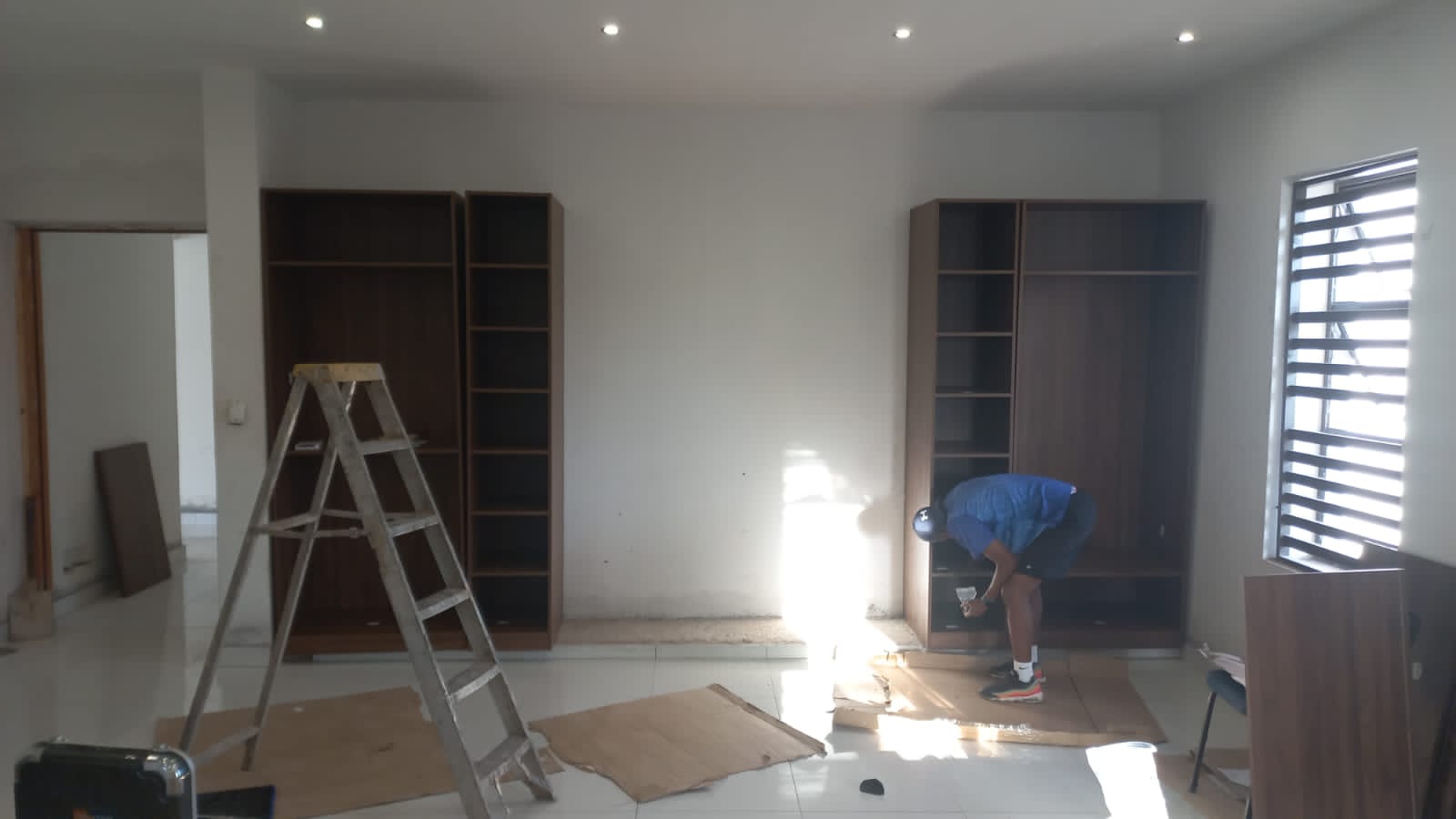 Installer fitting walnut-tone wardrobe carcasses in a bedroom