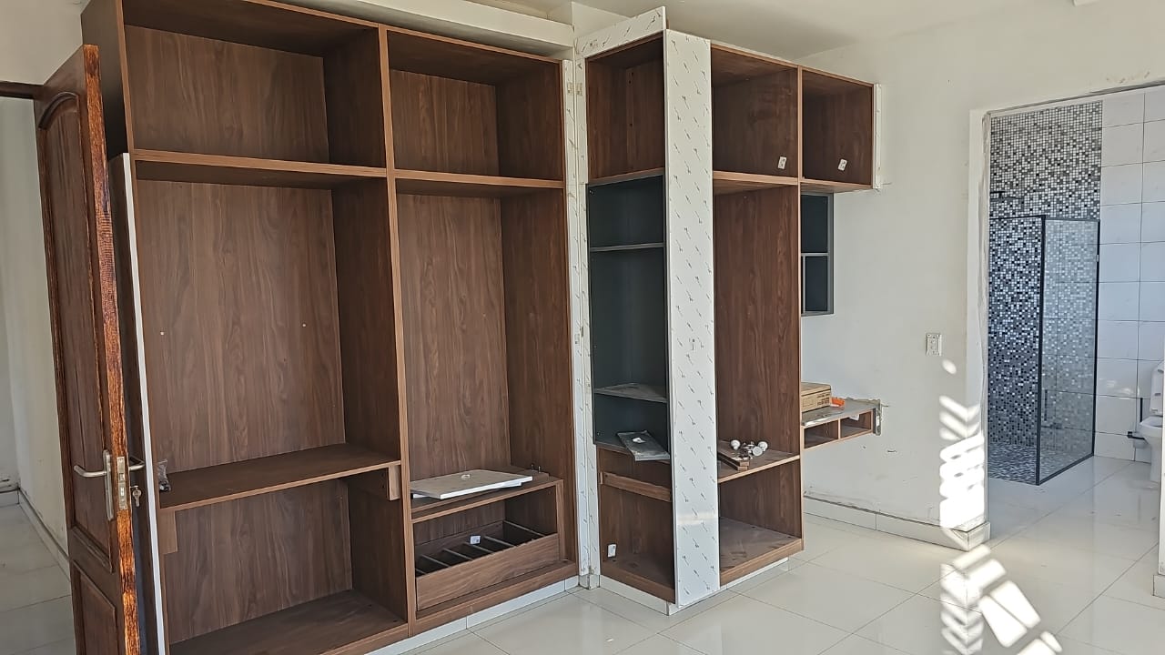 Walnut-tone built-in wardrobe carcasses with drawers beside a bathroom
