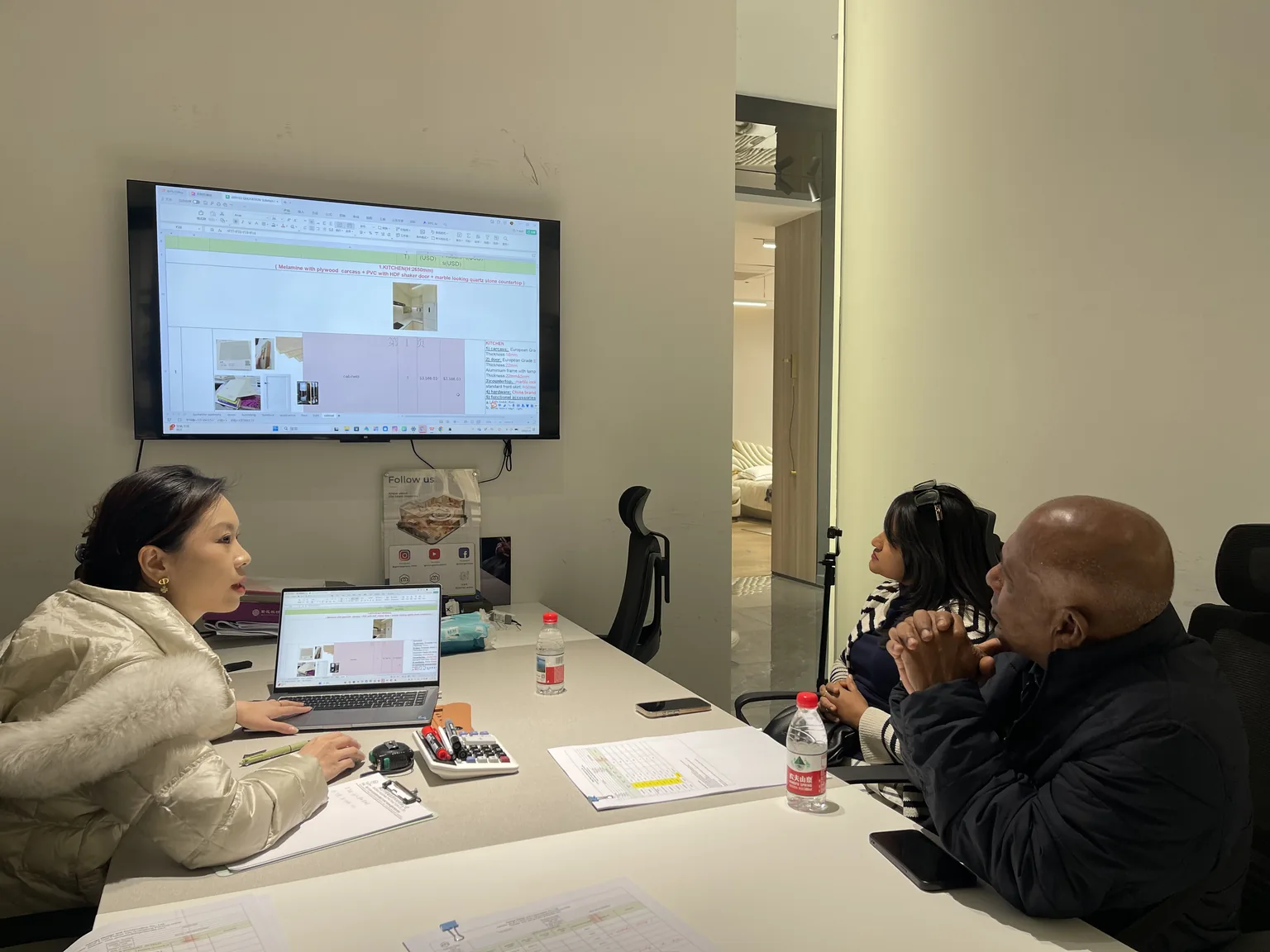 A George Group sales engineer reviewing a kitchen quotation and spec sheet with visiting buyers in a meeting room.