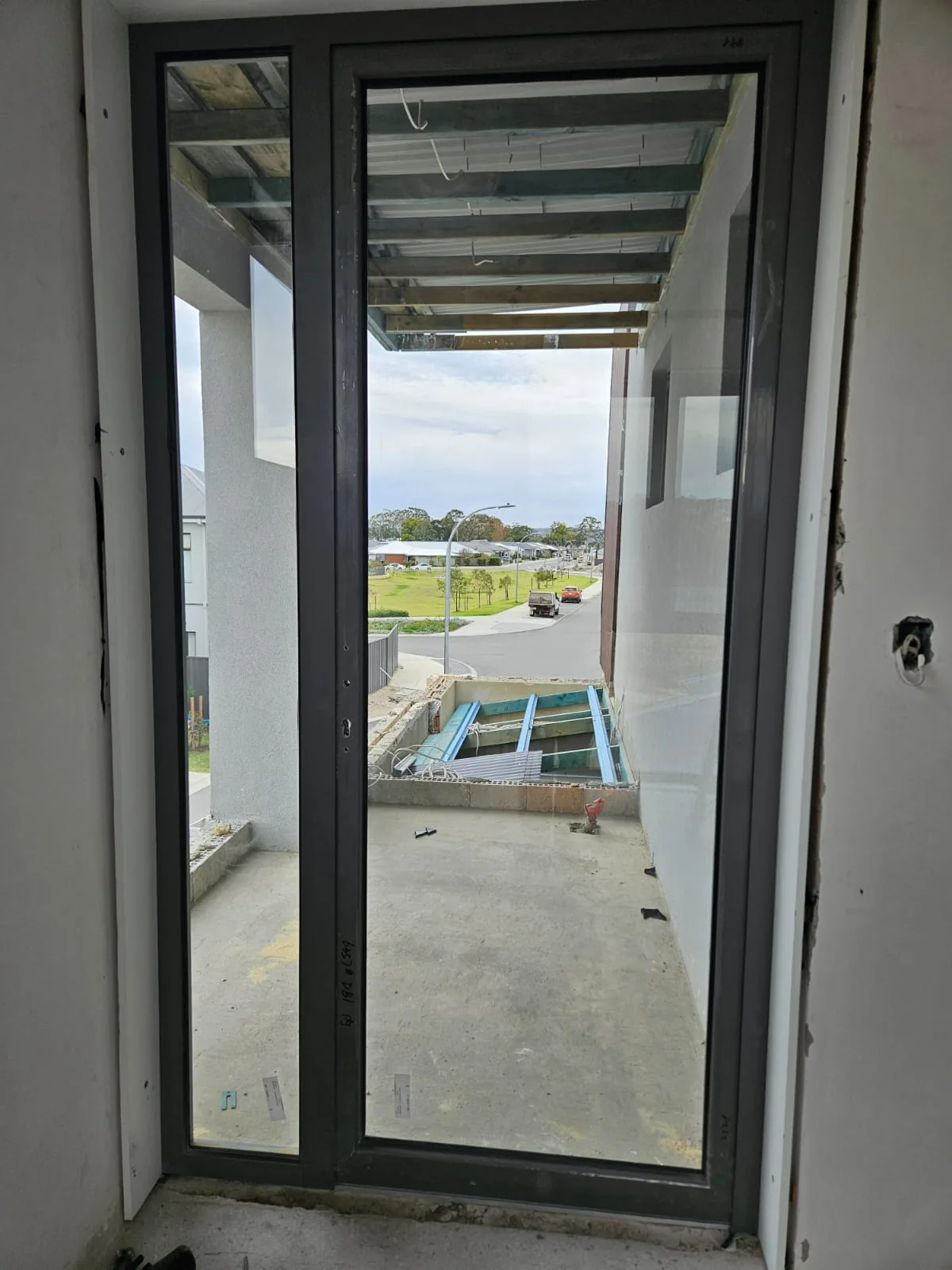 Installed dark-framed full-glass door on a residential construction site, viewed from inside toward the street