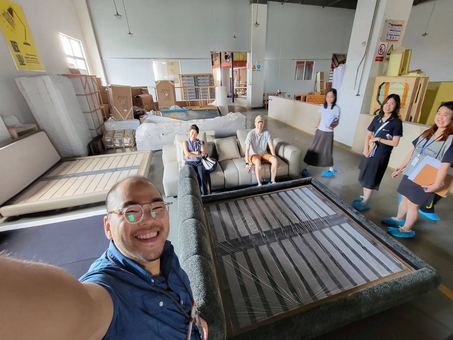 Visiting buyers testing a sofa during a factory tour at George Group's facility, with packed orders ready for shipment in the background.