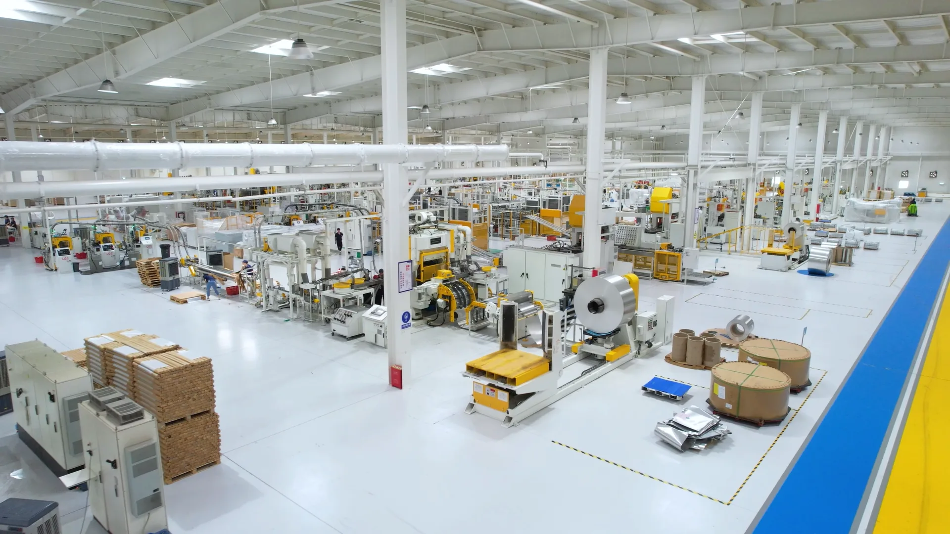Wide view of a George Group manufacturing facility in Foshan: a bright high-ceilinged production floor with rows of automated roll-fed machinery, stacked pallets of materials and marked walkways.